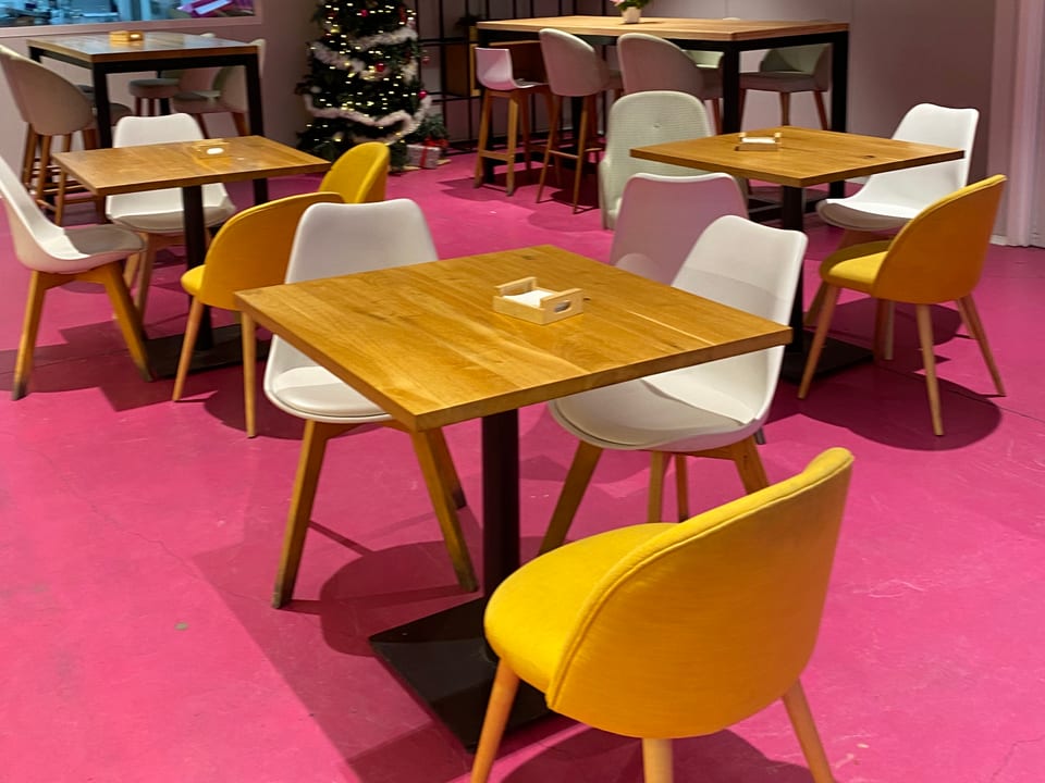 Zona de mesas de la cafetería de Ajalvir con suelo magenta y luces cálidas