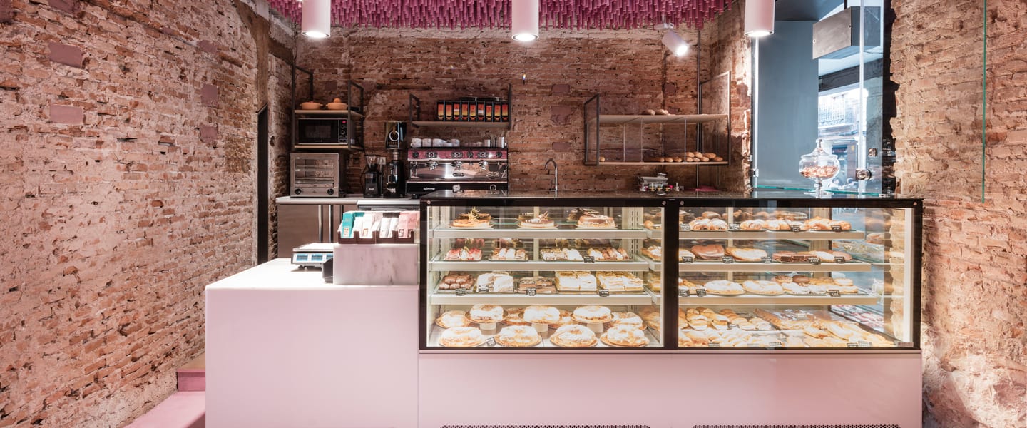 El mostrador: la vitrina llena de bollería y pastelería bajo el rótulo, con el frente rosa de la marca