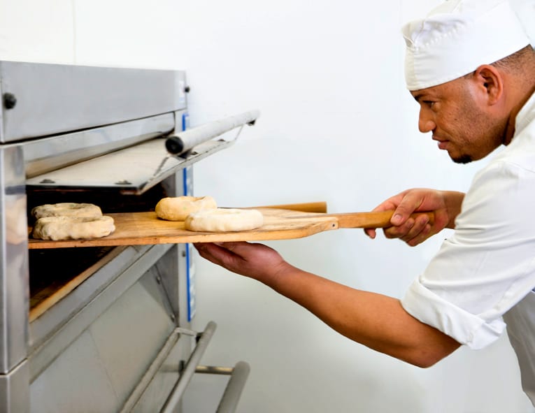 Un panadero introduce las piezas en el horno con la pala de madera